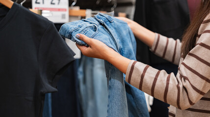 Woman comparing blue jeans in a clothing store - shopping decision and consumer behavior concept