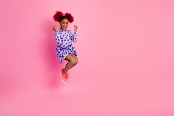 Joyful young girl leaps in a purple polka dot dress against a pink backdrop showcasing fun fashion and carefree childhood energy