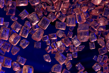 Macro close-up of pink Himalayan salt crystals scattered on a dark background with blue light. Food, seasoning, gourmet, health, and mineral concept.