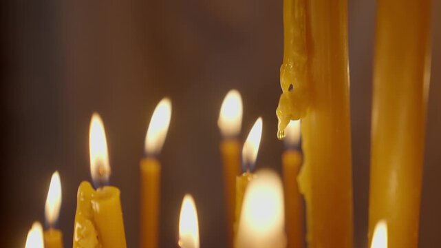 Long white religious candles, flames burning in the church. Close up shot of burning candle on dark background in church with no people