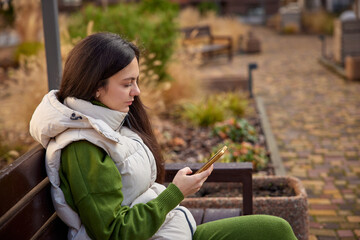 Woman sitting on a park bench, texting on her mobile phone