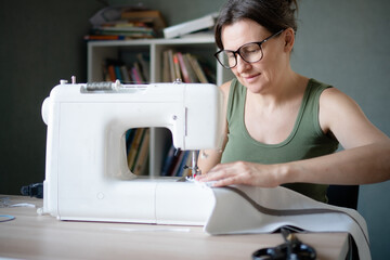 Close up portrait of a concentrated and engaged female seamstress working at her sewing machine in...