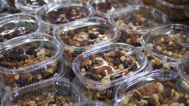 Closeup of a large array of transparent plastic containers neatly arranged in a row, each filled with a vibrant mix of nuts and dried fruits like hazelnuts, peanuts, cashews, and raisins. 