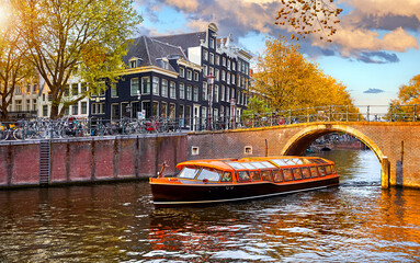 Channel in Amsterdam Netherlands. Pleasure boat by the bridge. Landmark old European city spring landscape with sunshine. Houses and trees over river Amstel.