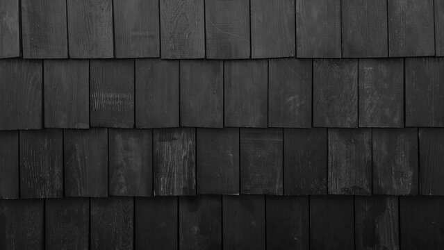 Old black rustic wood shingles texture background. Black weathered cedar shake wall siding. Grunge timber roof surface pattern with rough vertical grain details for architectural design.
