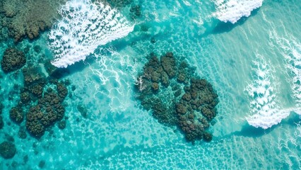 An aerial perspective reveals vibrant turquoise ocean waters with visible coral formations and white breaking waves.