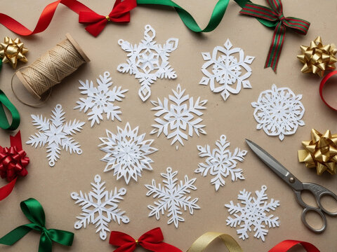 Flat lay of handcut paper snowflakes, colorful ribbons, twine and scissors on craft table, creative diy christmas project