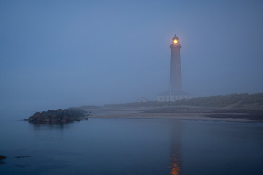 illuminated lighthouse skagen fyr with reflection on the coast of jutland denmark at blue hour in the morning