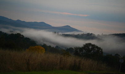 Autumn landscape above a village, cloudy sunset with fog and clouds in a mountain area.