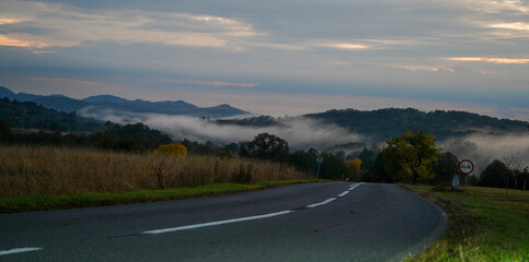 Autumn landscape above a village, cloudy sunset with fog and clouds in a mountain area.