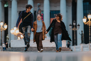 Three friends walk together on a city plaza at dusk, smiling and holding hands. They wear casual outfits and jackets, sharing a joyful moment amid warm street lights and grand columns.