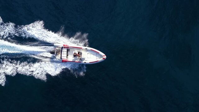 Aerial overhead view of a RIB motorboat crossing the ocean and leaving a trail of white waves and bubbles