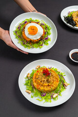 Korean bibimbap rice bowl topped with vegetables and a fried egg. Traditional, colorful dish arranged in a modern flat-lay food presentation.