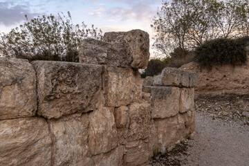 Weathered limestone blocks form a low fortress wall fragment at Zippori National Park in Galilee Israel. Archaeological heritage site at dusk with shrubs and a gravel path