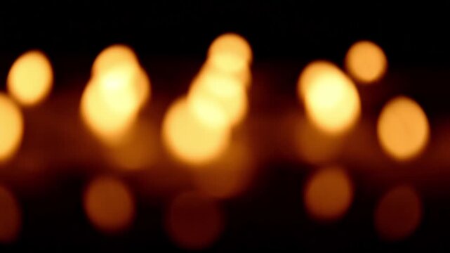 Defocused candle bokeh forms shifting warm orbs as light intensity changes , creating smooth motion in the blurred golden patterns of distant flames.
