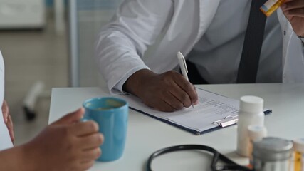 Black male physician writing in pregnant woman medical chart while providing guidance on proper medication use during prenatal consultation