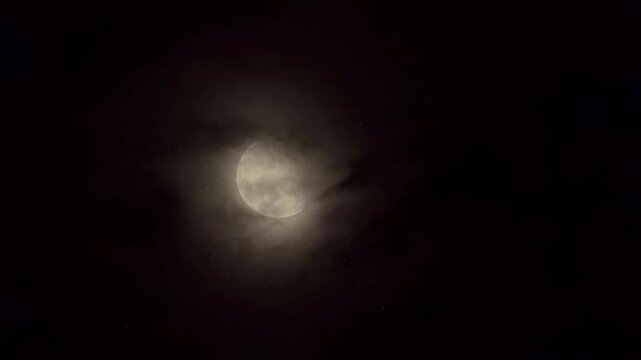 Half moon shining brightly behind passing clouds