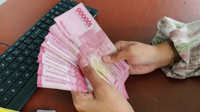 Female hands organizing rupiah bills near keyboard.