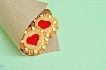 Shortbread cookies with red heart shaped jelly in the rolled vintage paper bag on the light green wooden table. Closeup of shortbread cookies