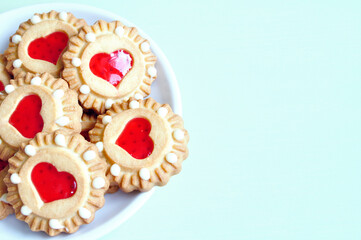 Shortbread cookies stuffed with red jelly in the form of hearts in the white saucer on the light green table, closeup of shortbread cookies