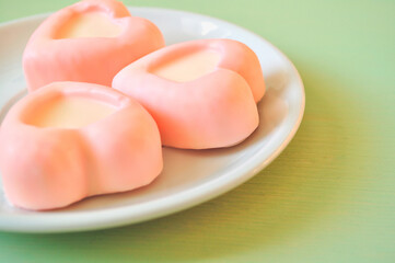 Souffle dessert, french souffle concept. Two heart-shaped pink souffle cakes lying on the white porcelain plate on the green wooden table. Selective soft focus on the cake.