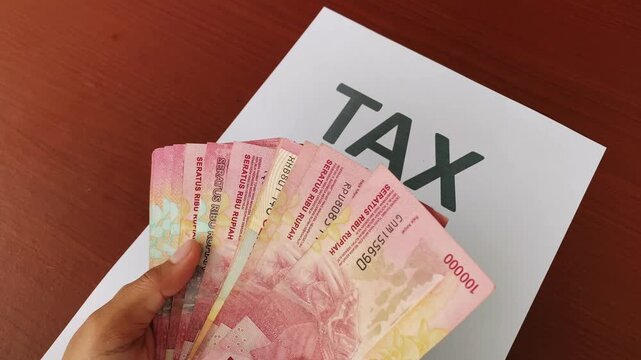 Indonesian rupiah held by a woman near tax document on office desk.