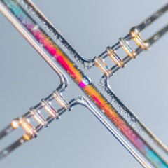 Macro of transparent microfluidic chip junction with iridescent dye flowing through cross channels on pale background. AI generative