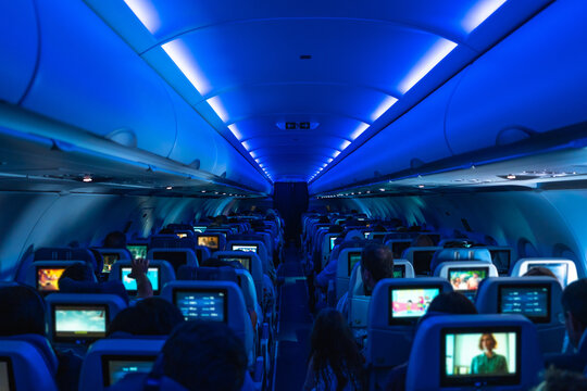 Passengers watching movies on individual screens in airplane cabin with blue ambient light