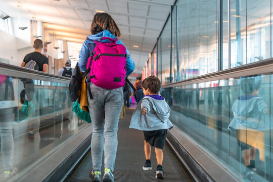 Mother and son walking on moving walkway in airport terminal - Powered by Adobe