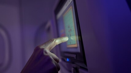 Passenger navigating in flight entertainment system, touching digital screen and browsing diverse media options while traveling at high altitude, exploring interactive content during journey