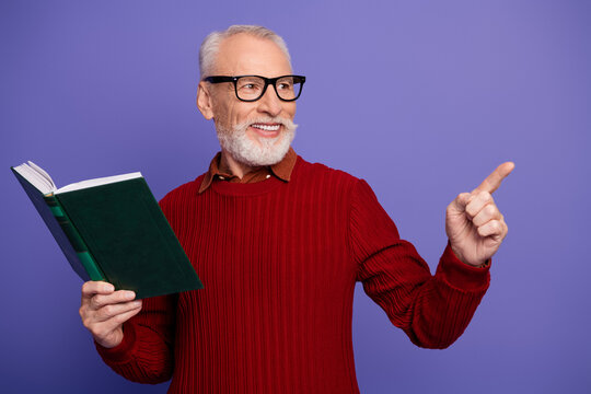 Mature gentleman reading a book in a red sweater smiling and pointing against a purple background