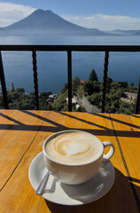 coffee cup on table with scenic view lake atitlan antigua guatemala blue water sunny volcano crater pond outdoor travel tourism adventure getaway cappuccino late milk cafe restaurant flavor santa cruz