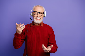 Mature male pensioner with headset smiling in a red sweater against a purple background for...