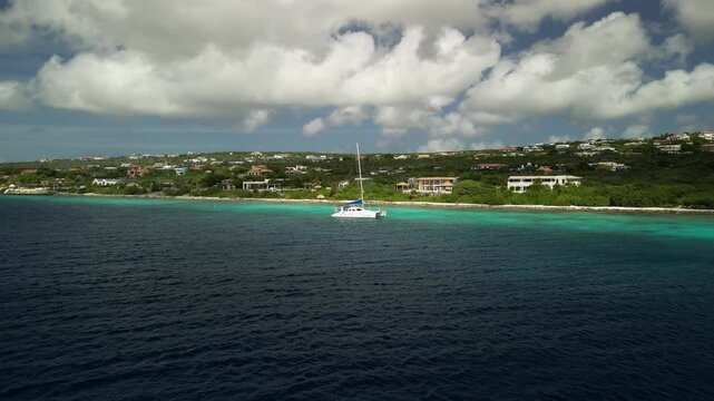 Drone footage showing a catamaran floating above vibrant reef water at Andrea Coastline, framed by clear skies and calm sea