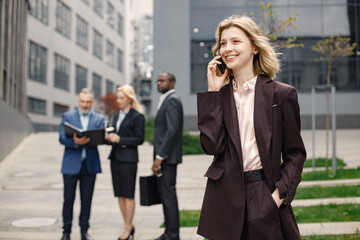 Blonde businesswoman standing and talking on the phone in front of modern office