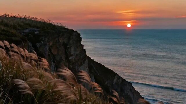 This fluid panning sequence starts with a close focus on the tough wild grasses swaying in the wind atop the rugged cliff, their blades glowing golden under the late-afternoon sun. The camera then gli
