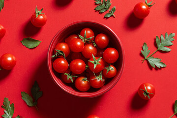 Artistic culinary arrangement with red cherry tomatoes forming a visually appealing pattern. Tomatoes displayed in a red bowl against a crimson background, emphasizing freshness and vegan-friendly