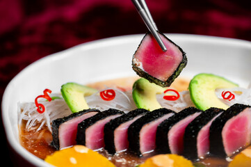 Seared tuna tataki appetizer with avocado and daikon radish in a white bowl, being served with chopsticks. Healthy Japanese seafood dish close-up