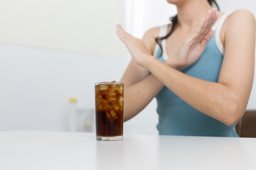 Woman making an X sign with hands in front stop of soda, promoting no sugar lifestyle and healthy drink awareness. Great for diet and wellness visuals.