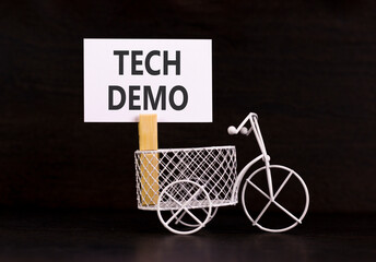 Tech demo symbol. Concept word Tech demo on beautiful white paper. Beautiful wooden clothespin. Miniature white bicycle. Beautiful black background. Business tech demo concept. Copy space.