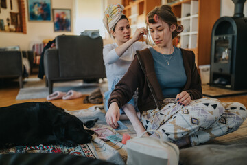 Two friends share a casual, at-home grooming moment. One woman styles the others hair with rollers as a calm dog lounges nearby, creating a warm, everyday domestic scene.