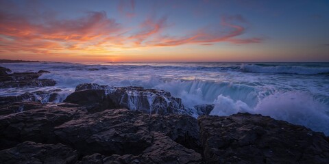 Waves breaking against rocks during sunset on shoreline, natural erosion risk