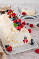 Meringue Pavlova roll cake with cream and fresh berries on top on a ceramic board on a concrete background. Copy space.