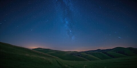 Obraz premium Meteor shower in the evening sky with falling stars over green hills, ideal for a celestial-themed background