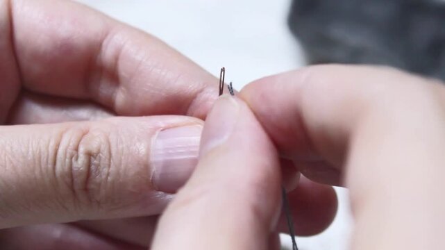 Man threading a needle with fingers in close-up detail  