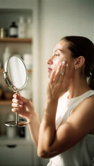 Young Woman Applying Face Cream Looking in Mirror