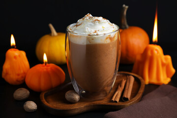 Delicious pumpkin latte with whipped cream and autumn decor on black background, closeup