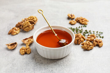 Honey in bowl, walnuts and thyme on light grey table, closeup