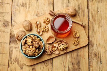 Delicious honey in glass jar, dipper and walnuts on wooden table, top view