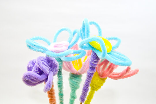 Colorful bouquet of handmade flowers crafted from pipe cleaners (fuzzy wires) in pastel and neon colors, against a white background. Concept for children's craft, DIY, and creativity.